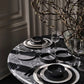 Dining table setting with black and white dishes, glasses, and decorative branches on a marble surface.