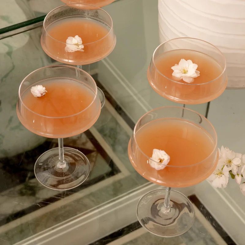 Four pink cocktails with white flowers on a reflective surface