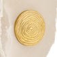 A round gold-toned wall plaque featuring concentric wood grain rings, displayed on a light beige stone surface.