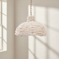 White beaded pendant light hanging against a neutral wall with sunlight casting shadows.