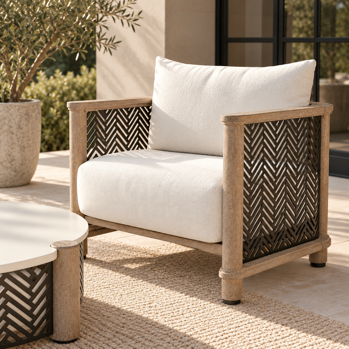 Outdoor armchair with a light wood frame, dark woven herringbone-pattern panels, and thick off-white cushions, shown on a patio next to a matching side table.