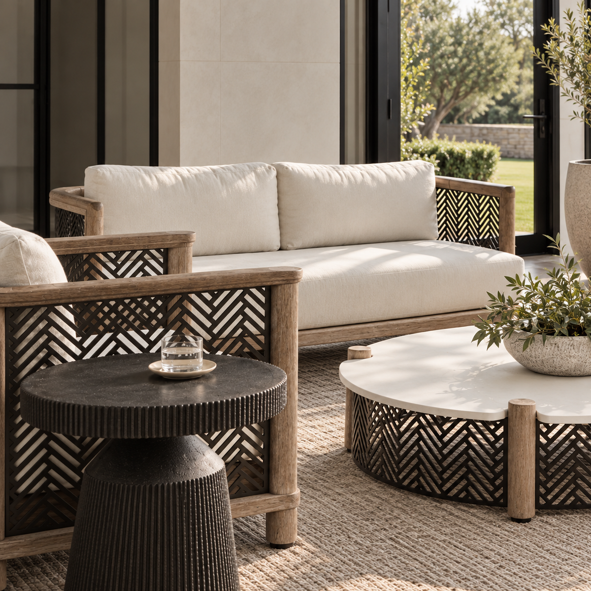 Outdoor patio furniture set featuring a wooden and woven rattan loveseat with off-white cushions, a matching armchair, a round white-top coffee table, and a small ribbed dark side table on a woven rug.