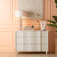 Beige dresser with decorative items against a peach-colored wall.