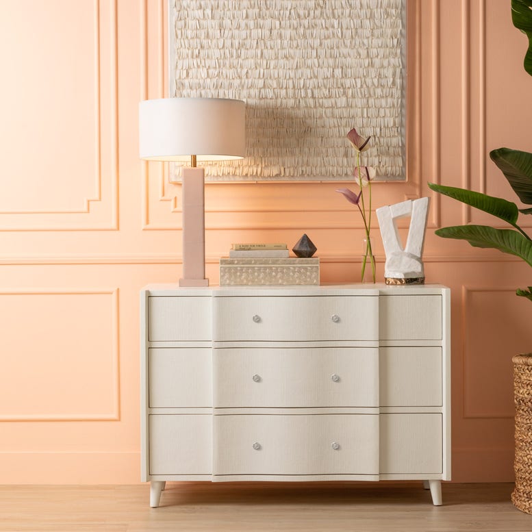 Beige dresser with decorative items against a peach-colored wall.