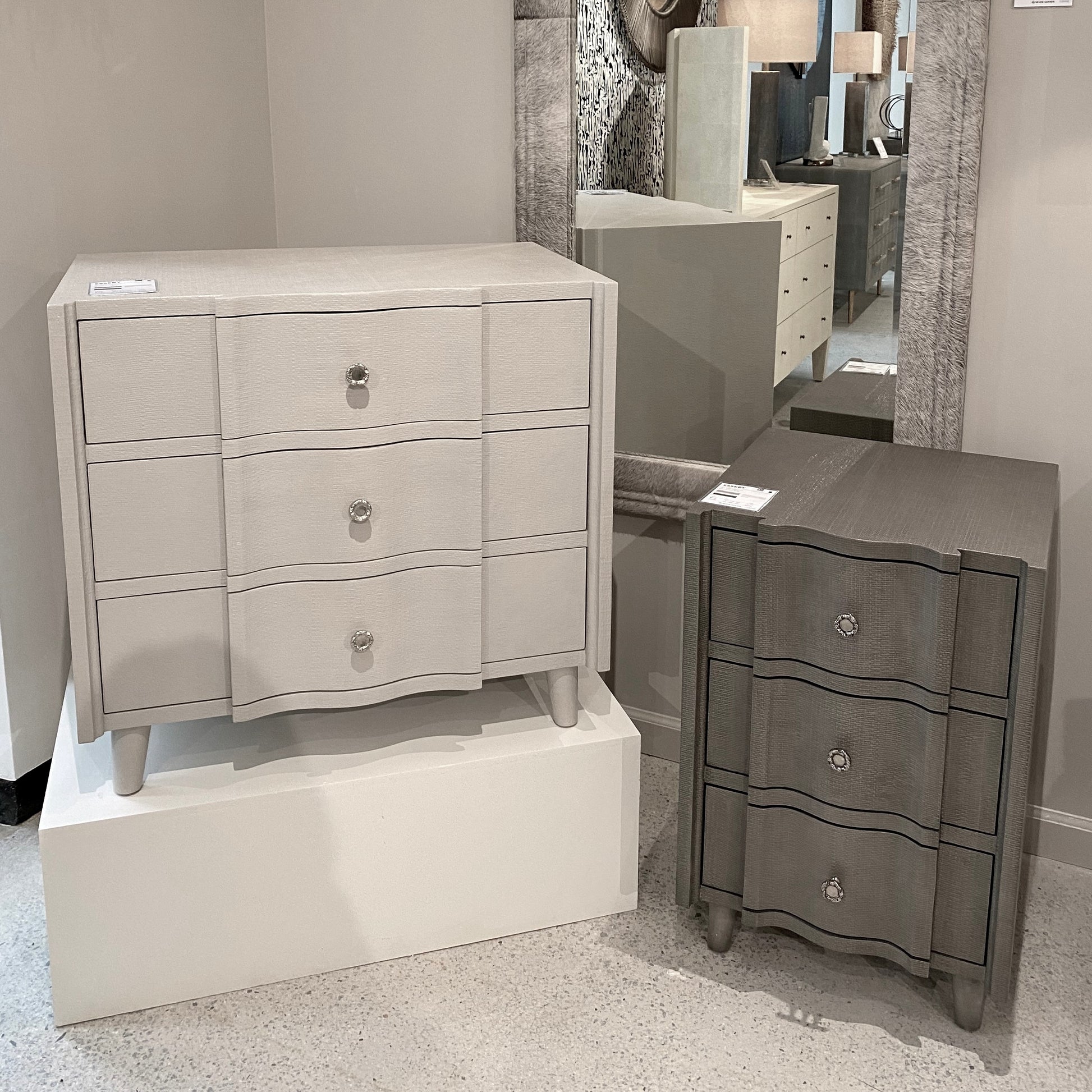 Two gray dressers with decorative handles in a showroom setting.