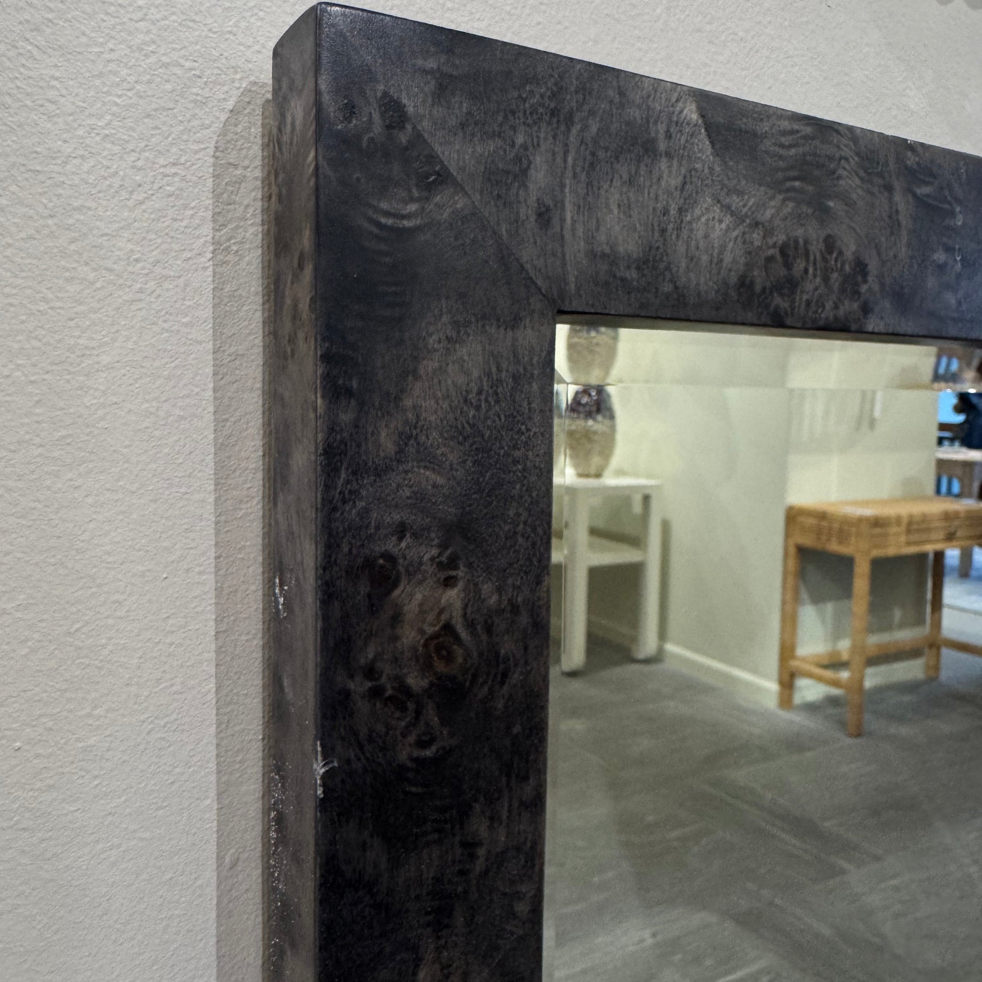 Close-up of a mirror with a dark wooden frame on a light-colored wall.