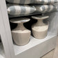 Two ceramic vases on a white shelf with striped cushions in the background.