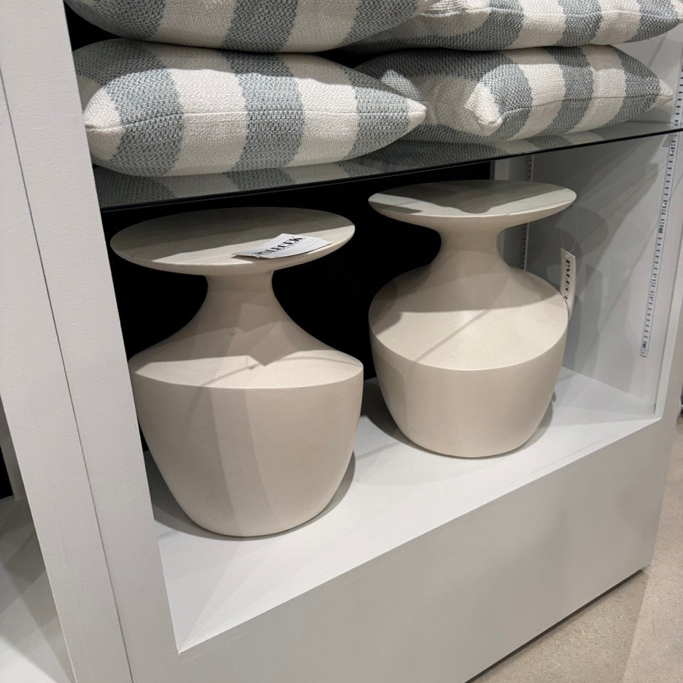 Two ceramic vases on a white shelf with striped cushions in the background.
