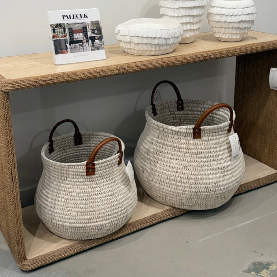 Woven baskets with wooden handles on a wooden shelf against a gray wall.