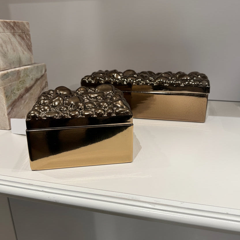 Two gold decorative boxes with textured lids on a white surface.