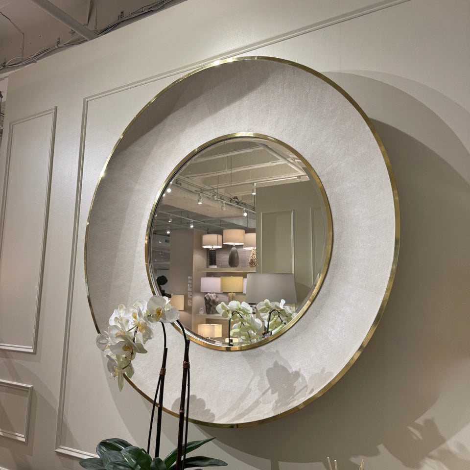 Round decorative mirror with a gold frame on a wall, with a plant and flowers in the foreground.