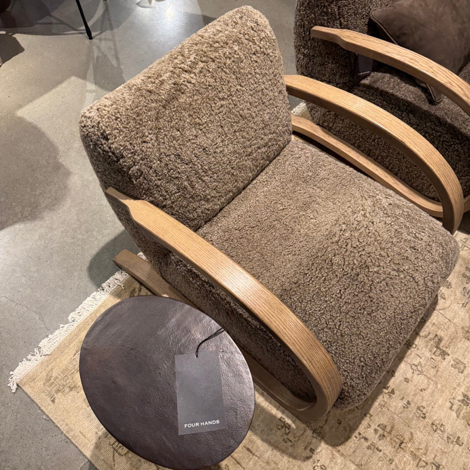 Brown upholstered armchair with wooden armrests and a matching ottoman on a patterned rug.