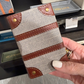 Hand holding a fabric phone case with brown leather accents in a store setting.