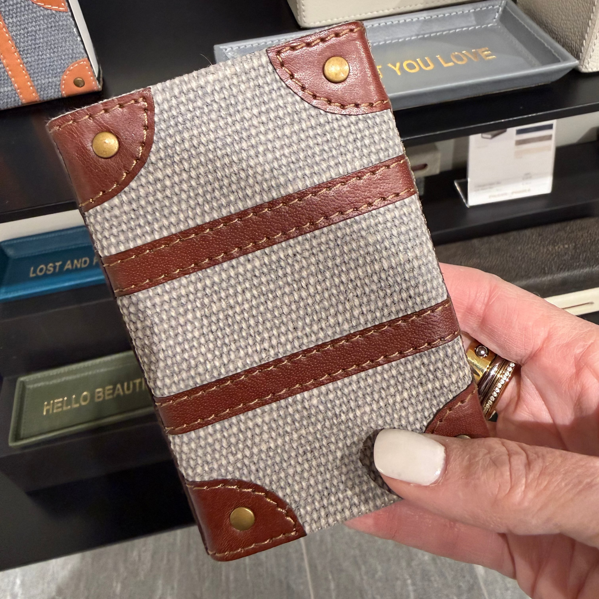 Hand holding a fabric phone case with brown leather accents in a store setting.