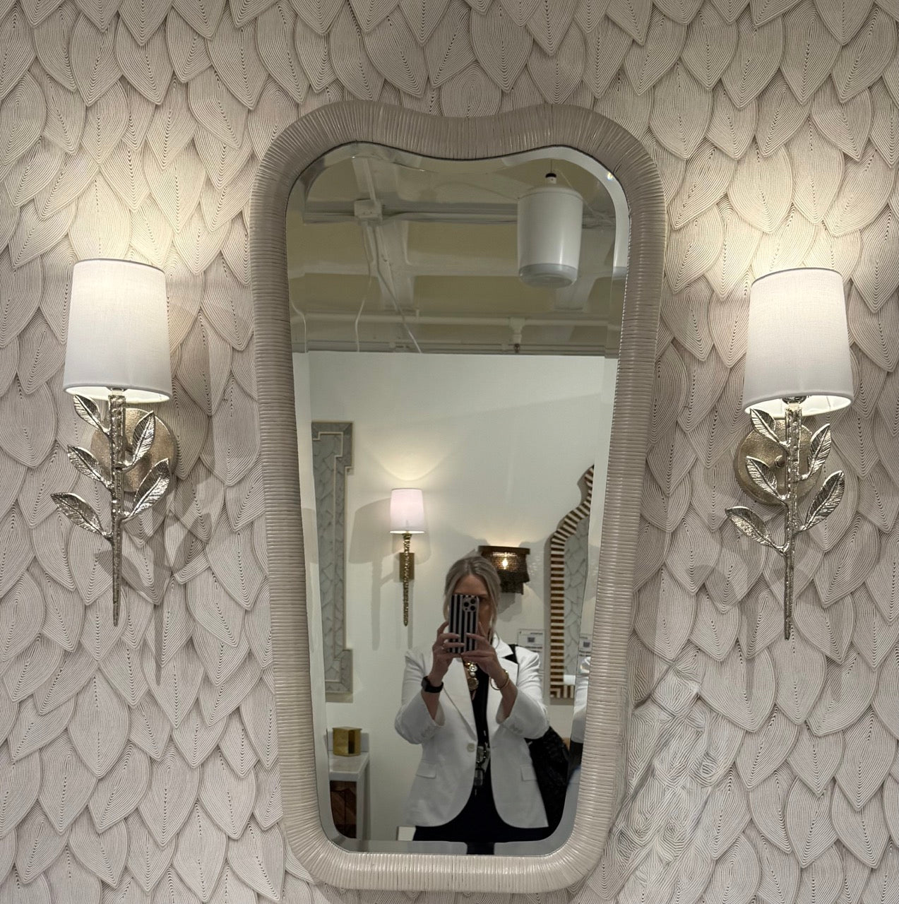 Person taking a mirror selfie in a room with decorative wall and lighting.