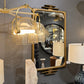 Decorative interior setting with a gold pendant light, mirror, and lamp on a gray wall.