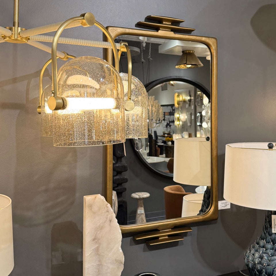 Decorative interior setting with a gold pendant light, mirror, and lamp on a gray wall.