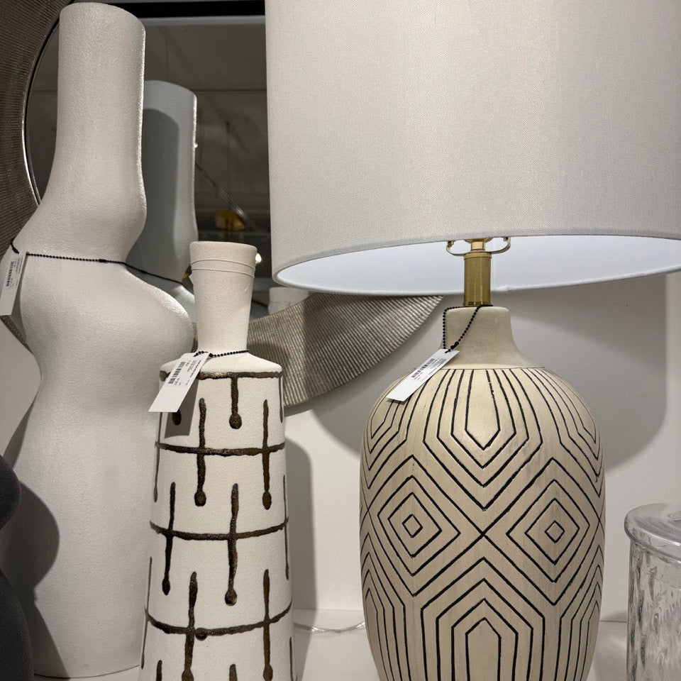 Two decorative vases with geometric patterns on a surface, with a lamp and mirror in the background.