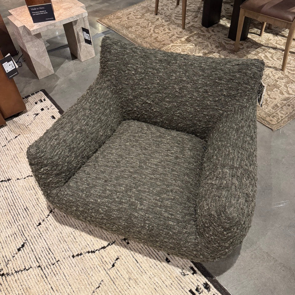 Gray textured armchair on a patterned rug with a dining area in the background