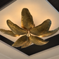 A modern ceiling light fixture shaped like metallic gold leaves, mounted on a white ceiling with dark trim.