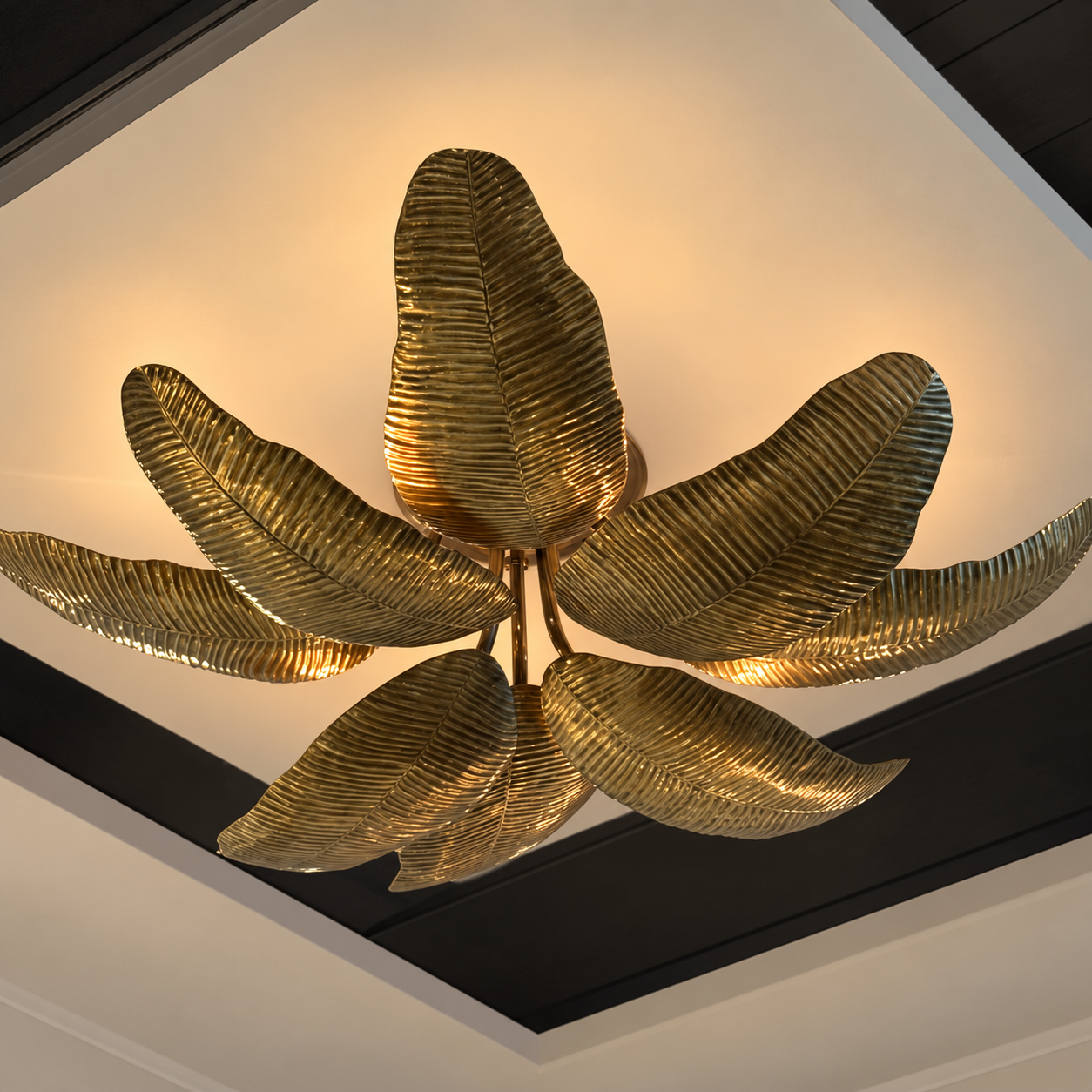 A modern ceiling light fixture shaped like metallic gold leaves, mounted on a white ceiling with dark trim.