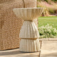 Decorative stone pedestal on a wooden deck with a woven basket and plants in the background