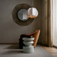 Modern interior with a round mirror, pendant light, and chair.