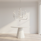 Modern white chandelier hanging above a round table in a minimalistic room.