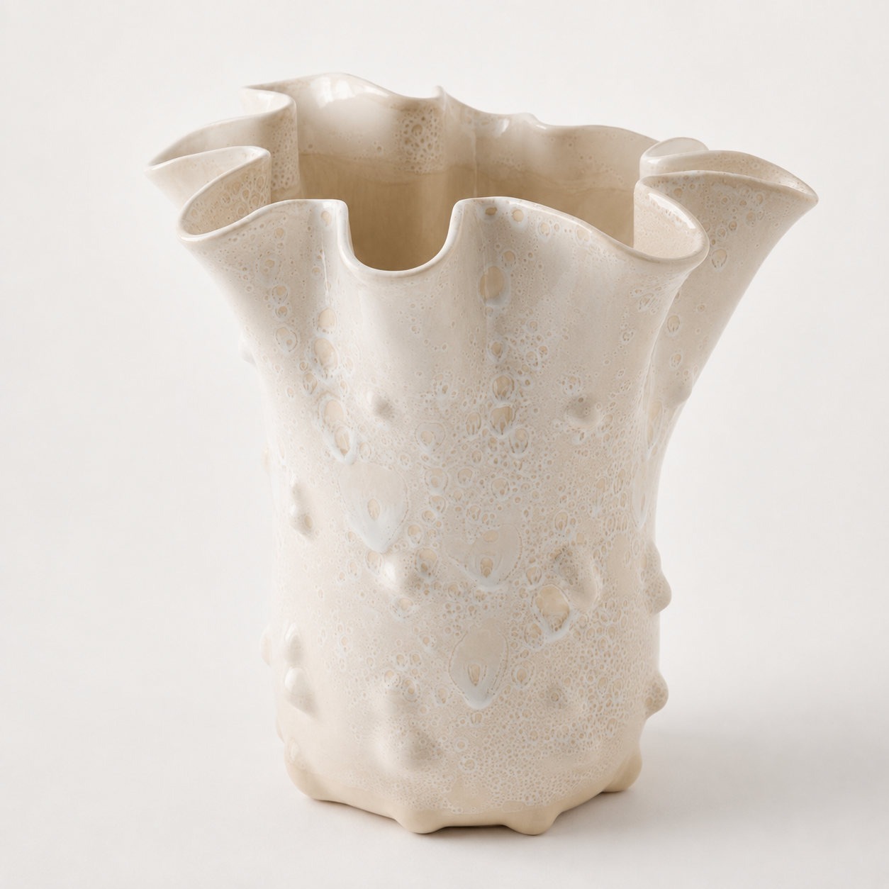 An organic-shaped ceramic vase with a textured, bubbly surface and flared, wavy rim, in a warm cream or off-white glaze against a light neutral background.