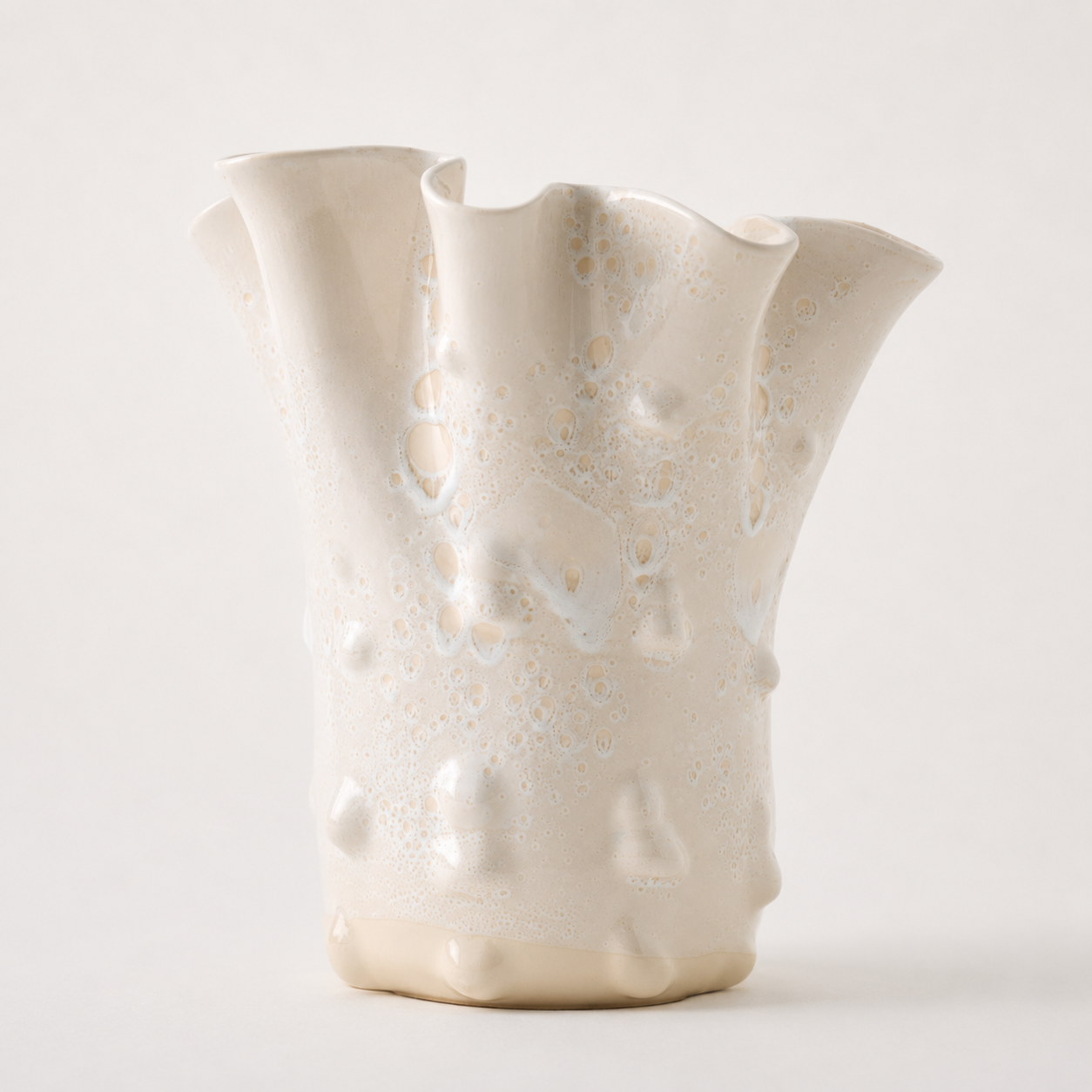 An organic-shaped ceramic vase with a flared, wavy rim and a glossy, textured surface featuring bubble-like patterns, in a warm cream or off-white color, set against a plain light background.