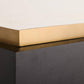 Close-up of a modern table corner showing a white marble top with a brushed gold metal edge, mounted on a dark charcoal wood base.