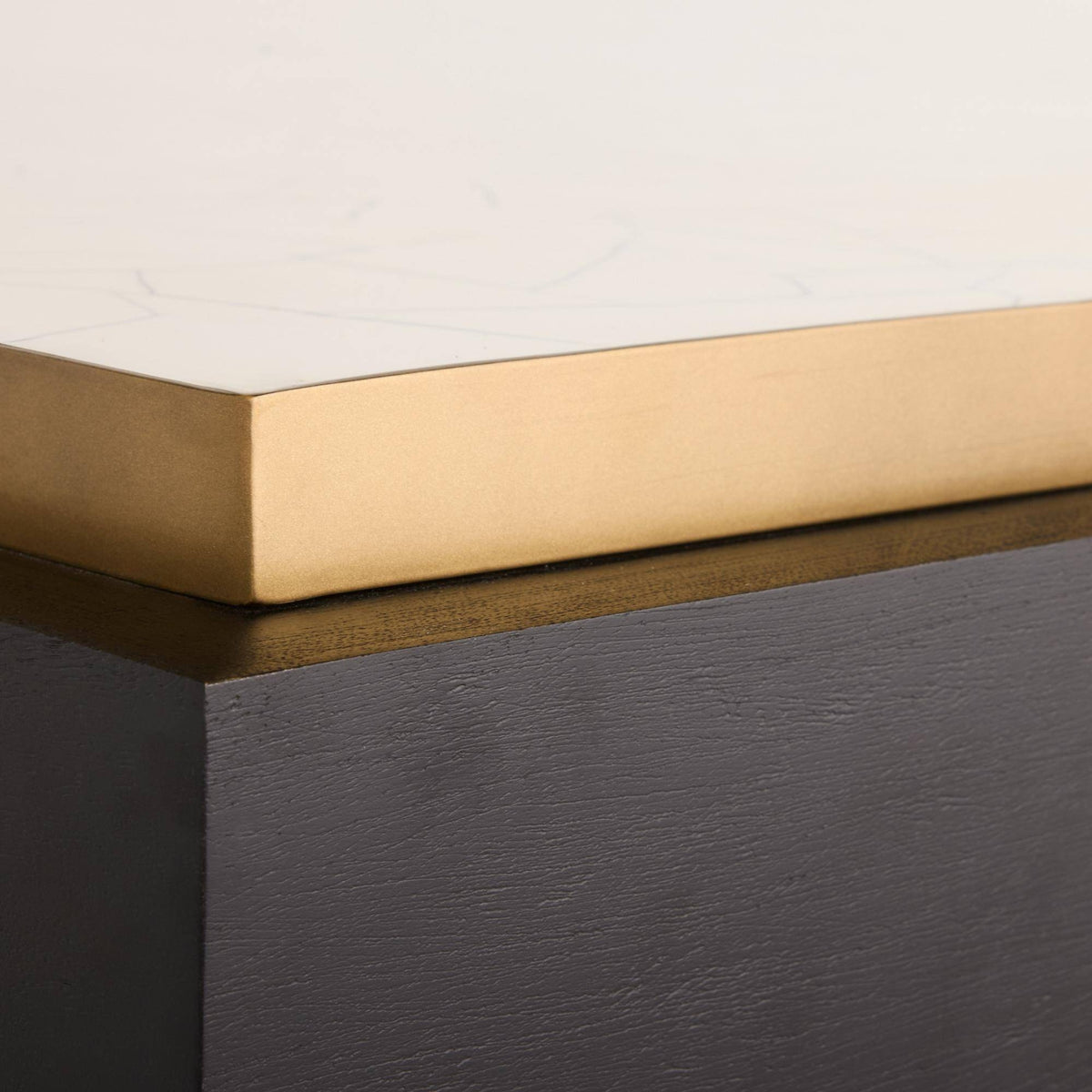 Close-up of a modern table corner showing a white marble top with a brushed gold metal edge, mounted on a dark charcoal wood base.