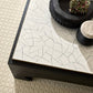Decorative coffee table with a cracked white surface and black base on a textured floor.