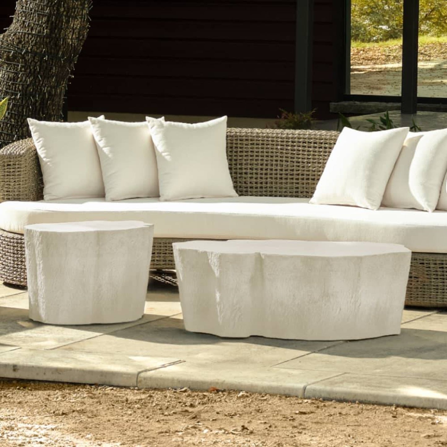 Outdoor patio set with wicker sofa and stone coffee tables on a sunny day.