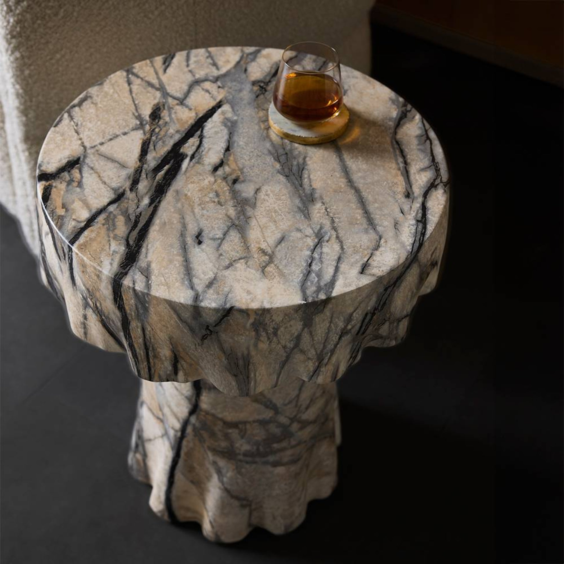 Marble-patterned side table with a glass of amber liquid on a dark background