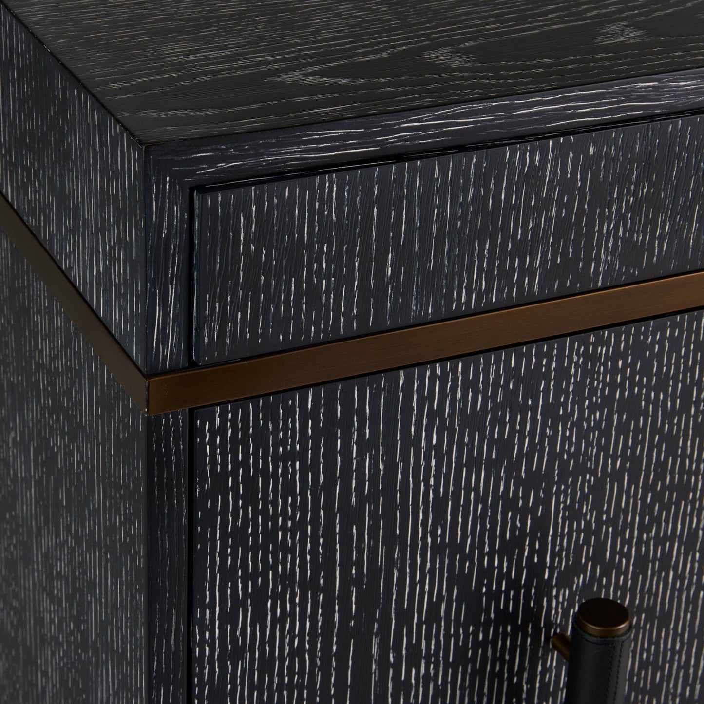 Close-up of a dark wood cabinet corner with a distressed black finish, a horizontal bronze metal accent strip, and part of a dark metal handle visible.