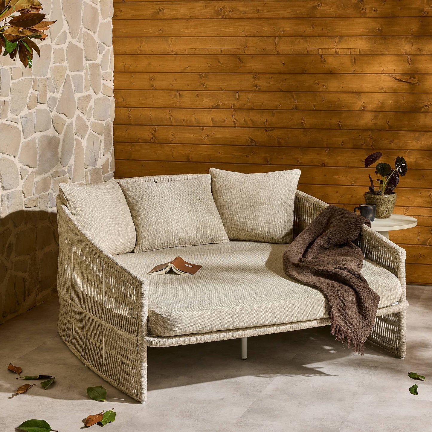 Beige outdoor sofa with cushions against a wooden wall.