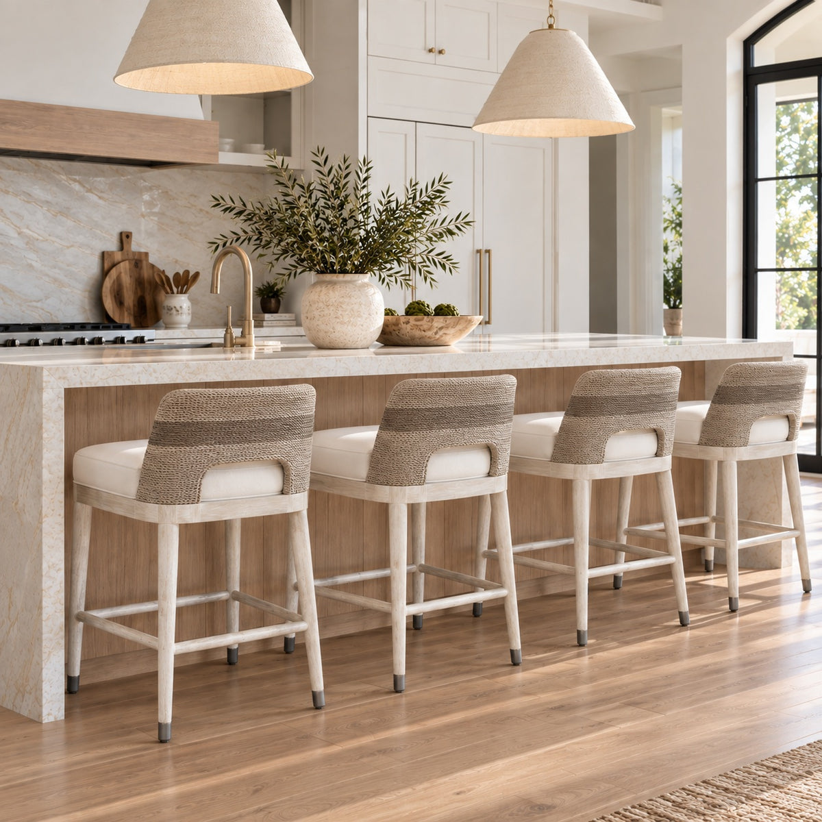 Four modern bar stools with woven beige backs and white seats, arranged along a light wood kitchen island in a bright, contemporary kitchen.
