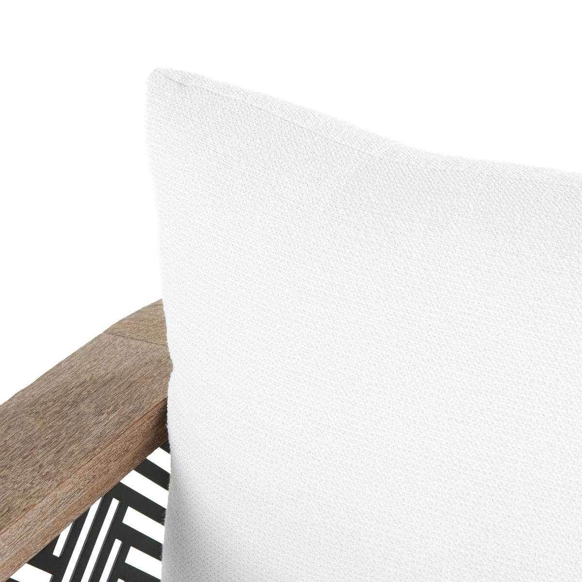 Close-up of a white pillow on a wooden chair with a black and white patterned rug.
