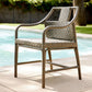 A high-back outdoor armchair with woven wicker-style seat and backrest, set on a patio beside a swimming pool.