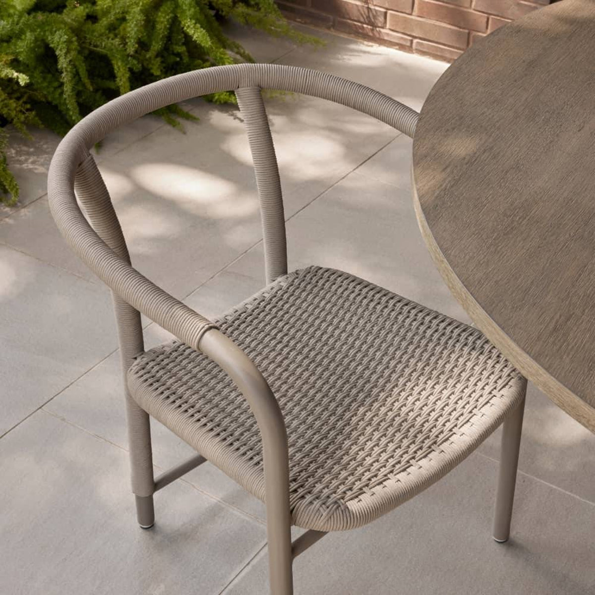 A modern outdoor armchair with a curved back and woven seat, shown next to a round table on a paved patio.