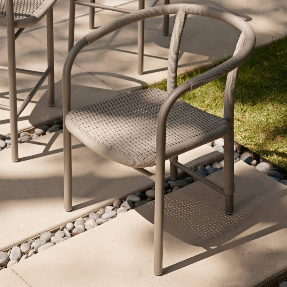 Beige outdoor chair on a patio with grass and stones in the background