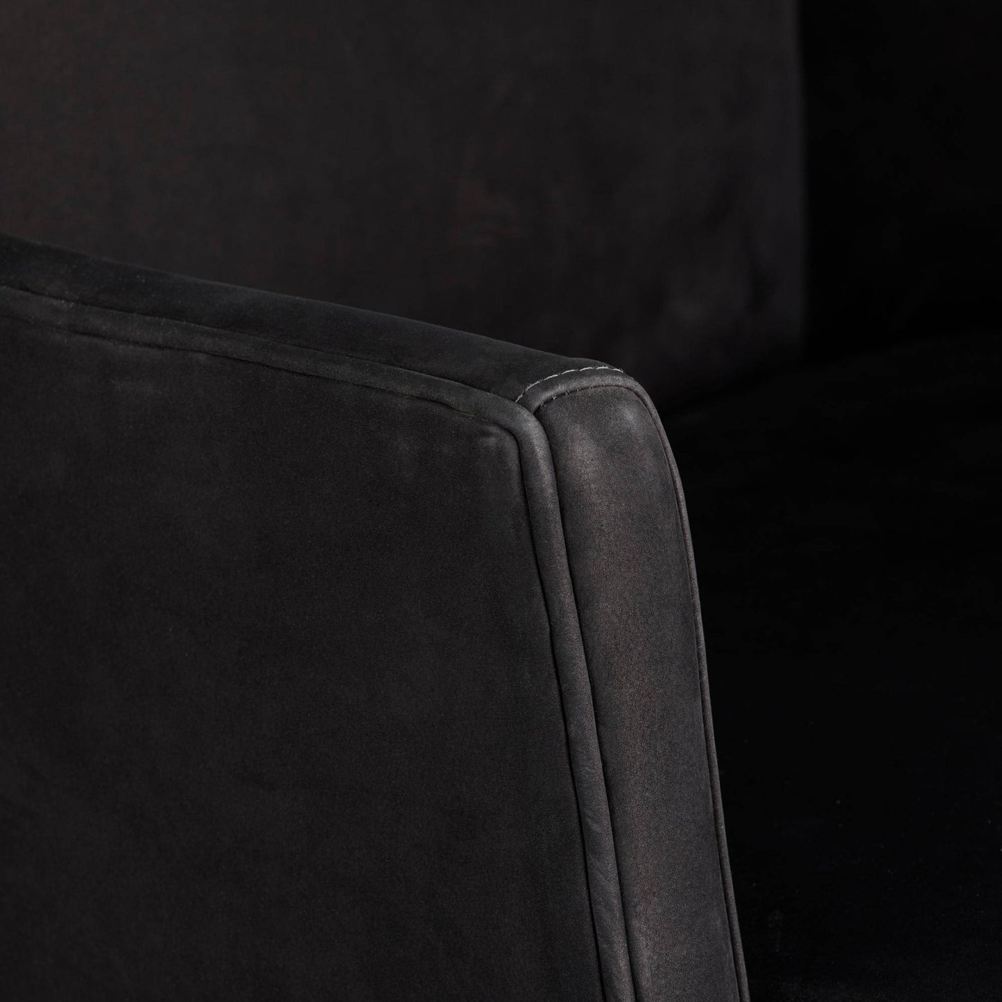 Close-up of a dark gray upholstered chair corner on a black background