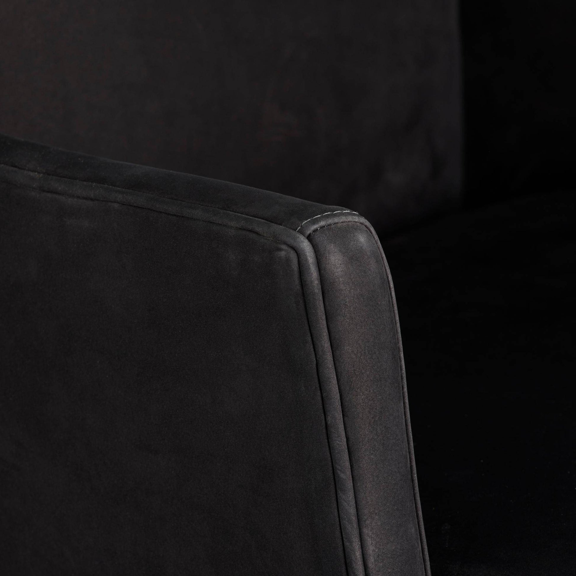 Close-up of a dark gray upholstered chair corner on a black background