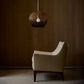 White armchair under a hanging woven lamp in a dimly lit room.
