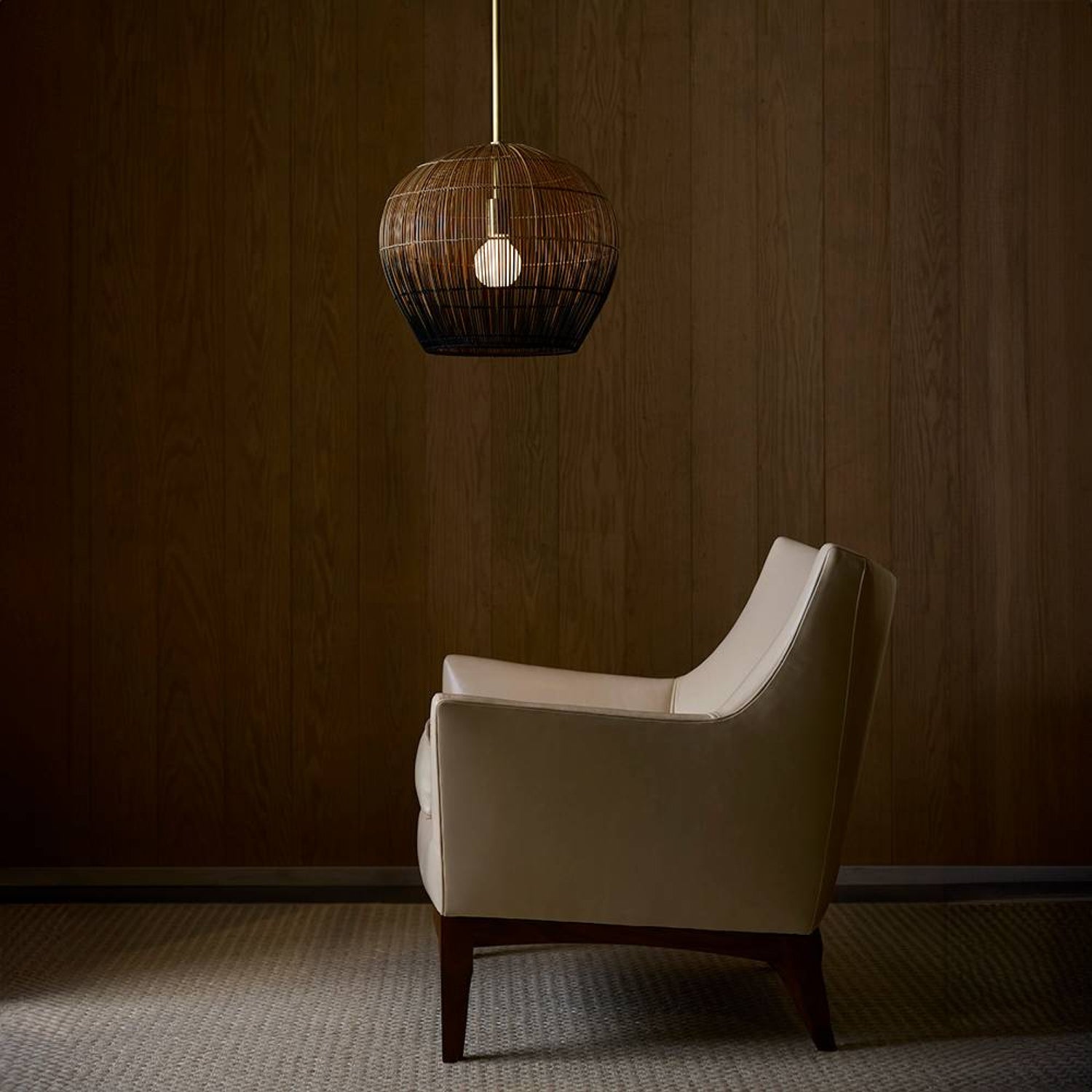 White armchair under a hanging woven lamp in a dimly lit room.