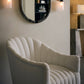 Modern beige armchair in a room with a mirror and wall lights.