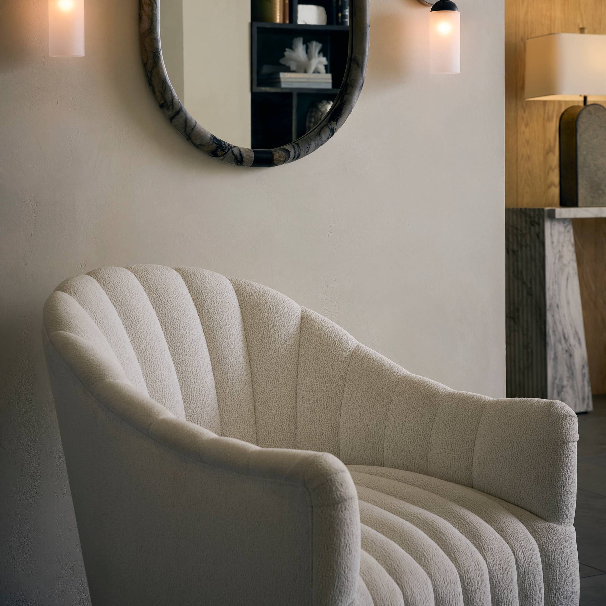 Modern beige armchair in a room with a mirror and wall lights.