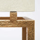 Close-up of a textured gold metal console table frame with a cream-colored pebbled stone or leather top, set against a plain white background.