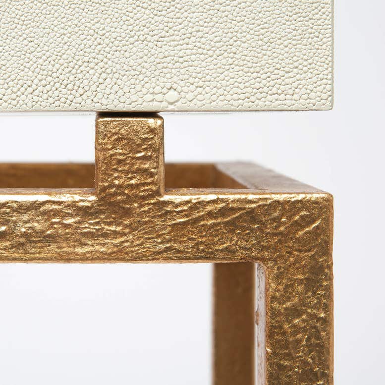 Close-up of a textured gold metal console table frame with a cream-colored pebbled stone or leather top, set against a plain white background.